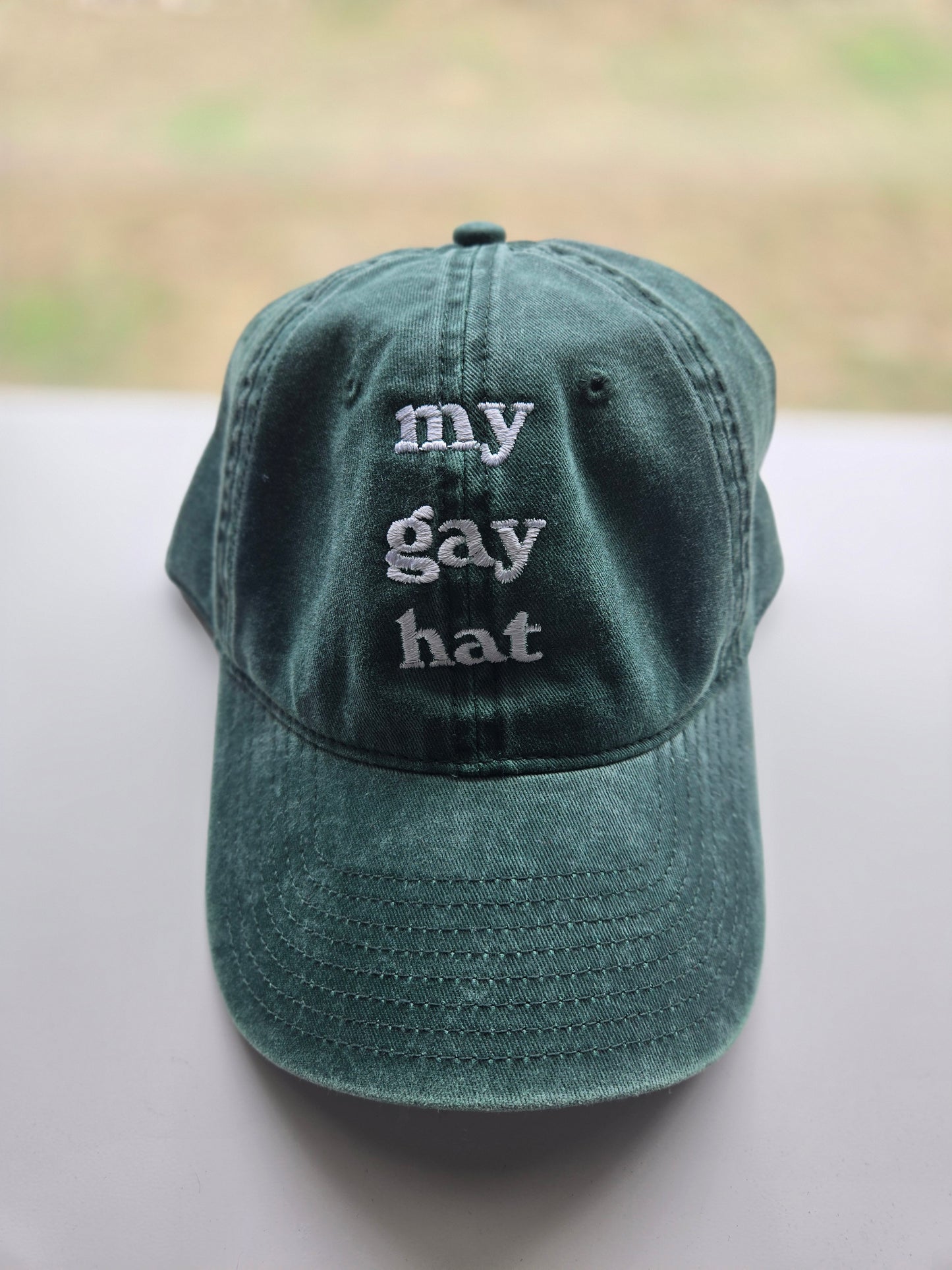 Vintage wash baseball cap with 'my gay hat' embroidered in white vintage-style font. Features a metal adjustable back and machine embroidery, designed by Carey Embroidery LLC."